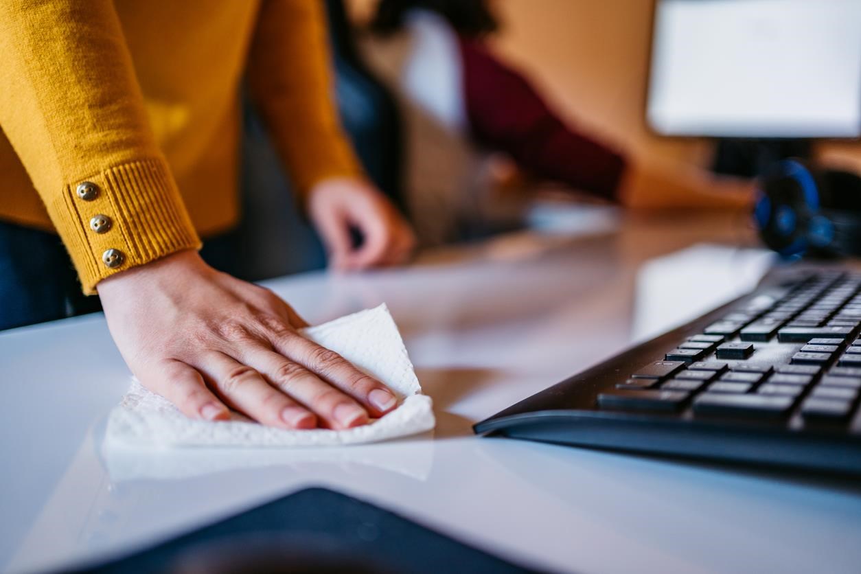 Woman wiping down a desk next to a keyboard. 