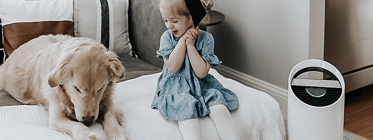 Little girl smiling at her dog, next to a TruSens Air Purifier. 